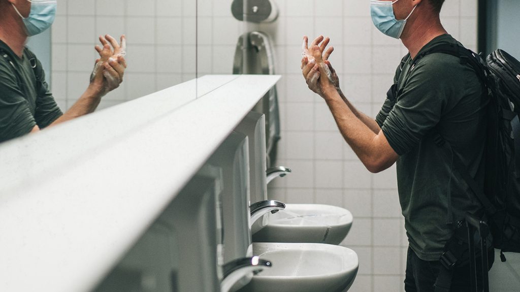 Pria yang memakai masker mencuci tangan di kamar mandi