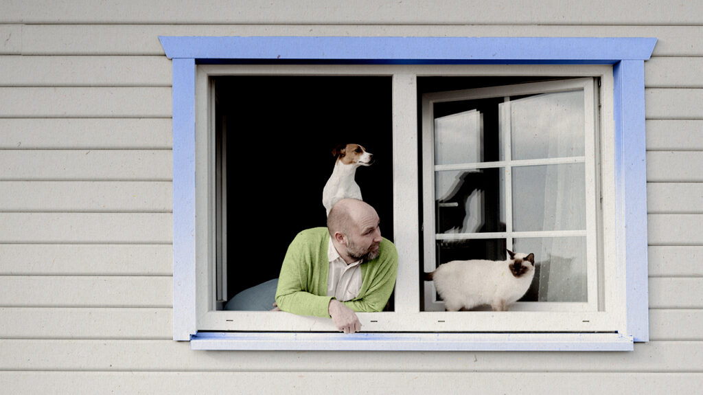 Keegi vaatab aknast välja, koer seljas ja kass kõrval