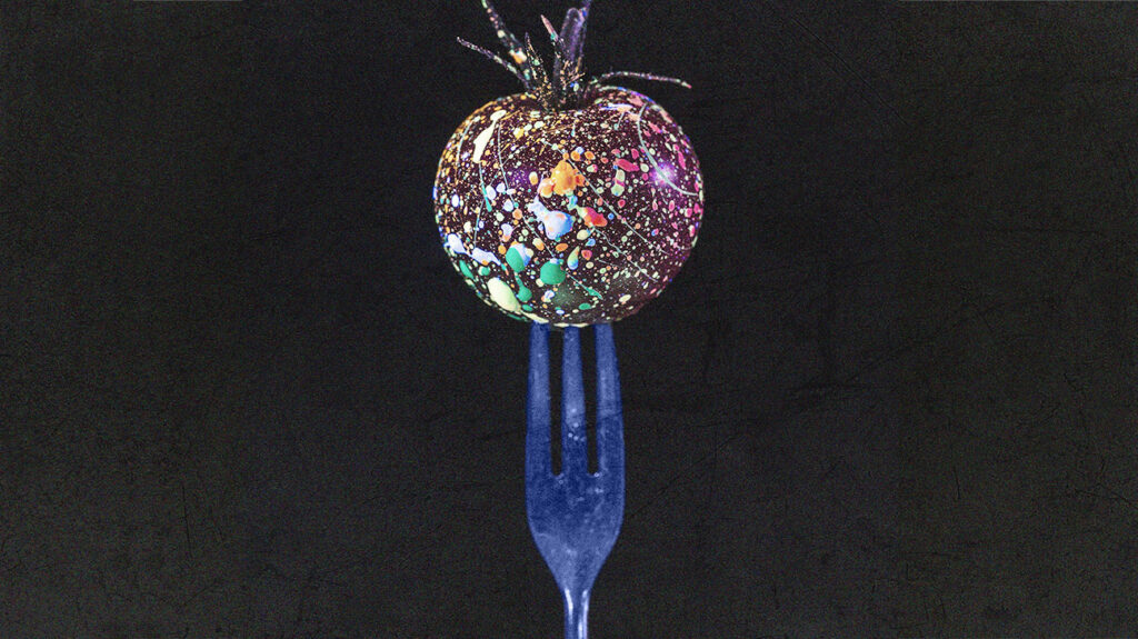 En liten cherrytomat på en gaffel, sprutet med neonfarger med mørk bakgrunn