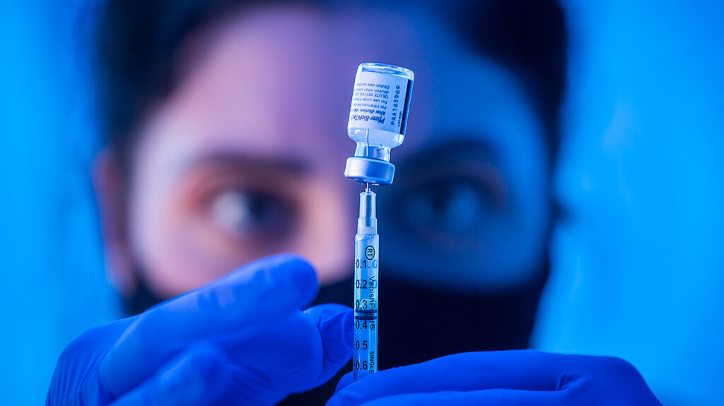close-up van de handen van de zorgverlener met de injectieflacon en de spuit met vaccin