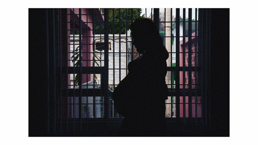Nėščia moteris stovi priešais langą pastato viduje.