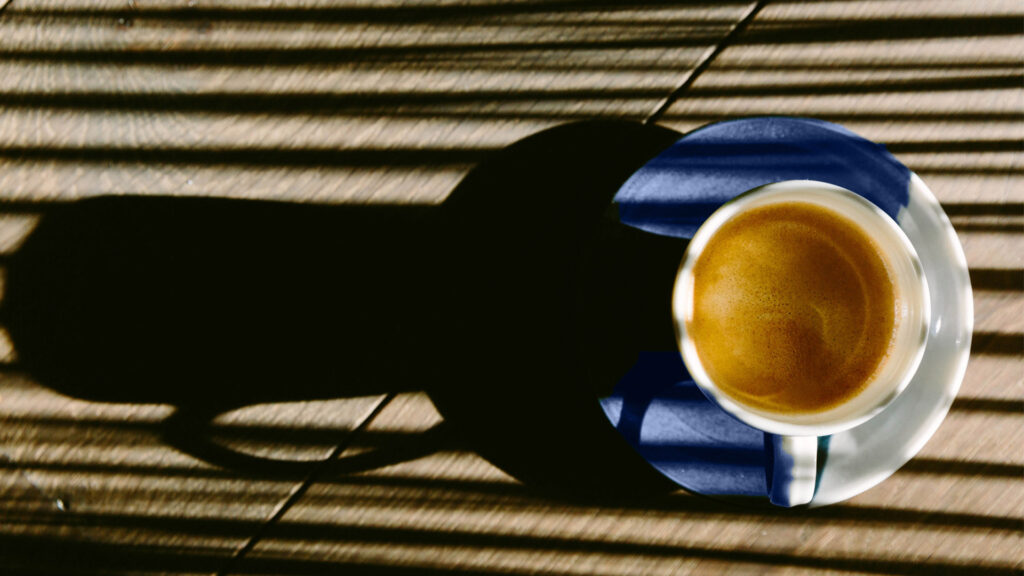 Puodelis kavos ant lėkštutės ir jos šešėliai saulės šviesoje